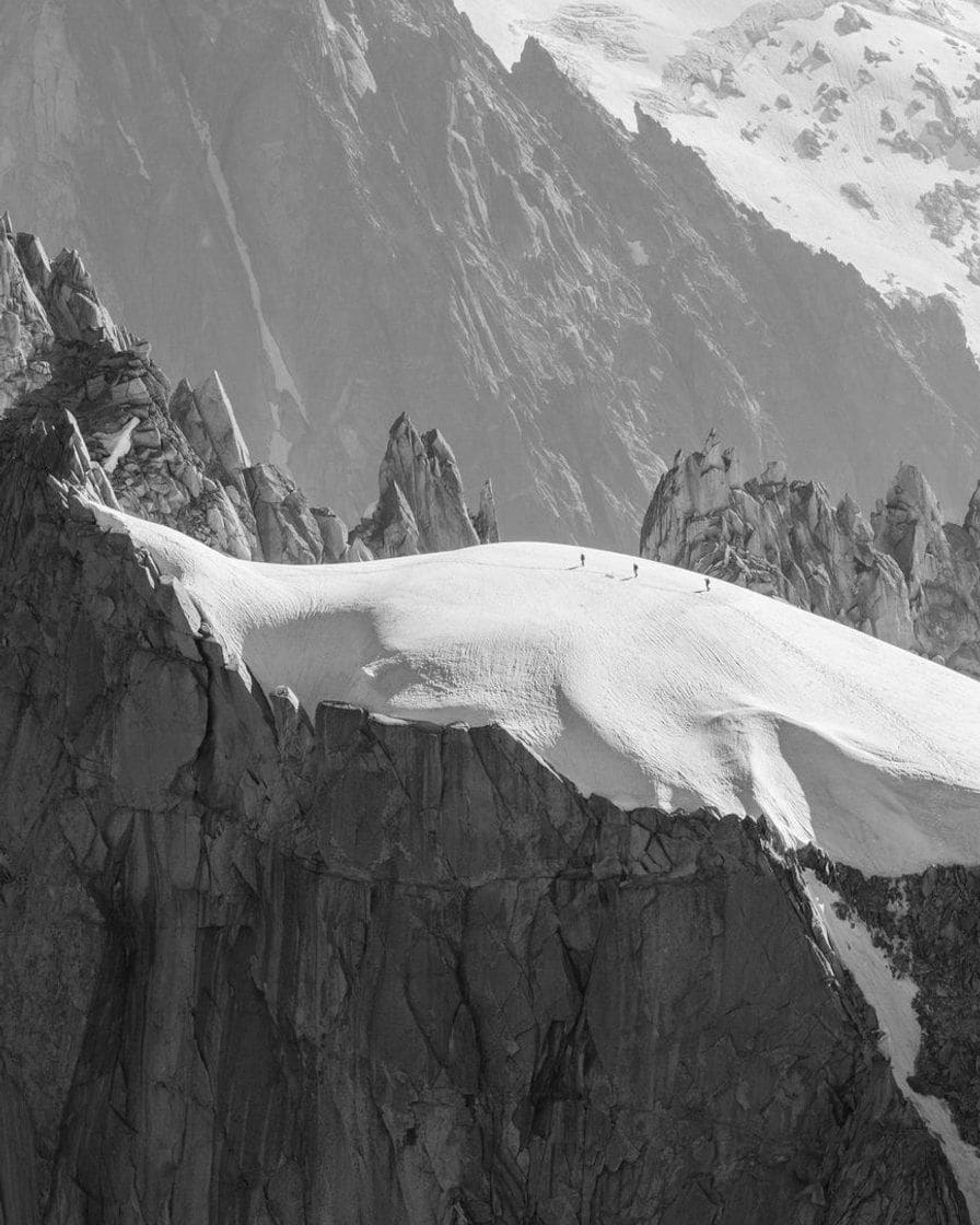 Alpinistes minuscules sur l'arête enneigée de l'Aiguille du Midi, en noir et blanc