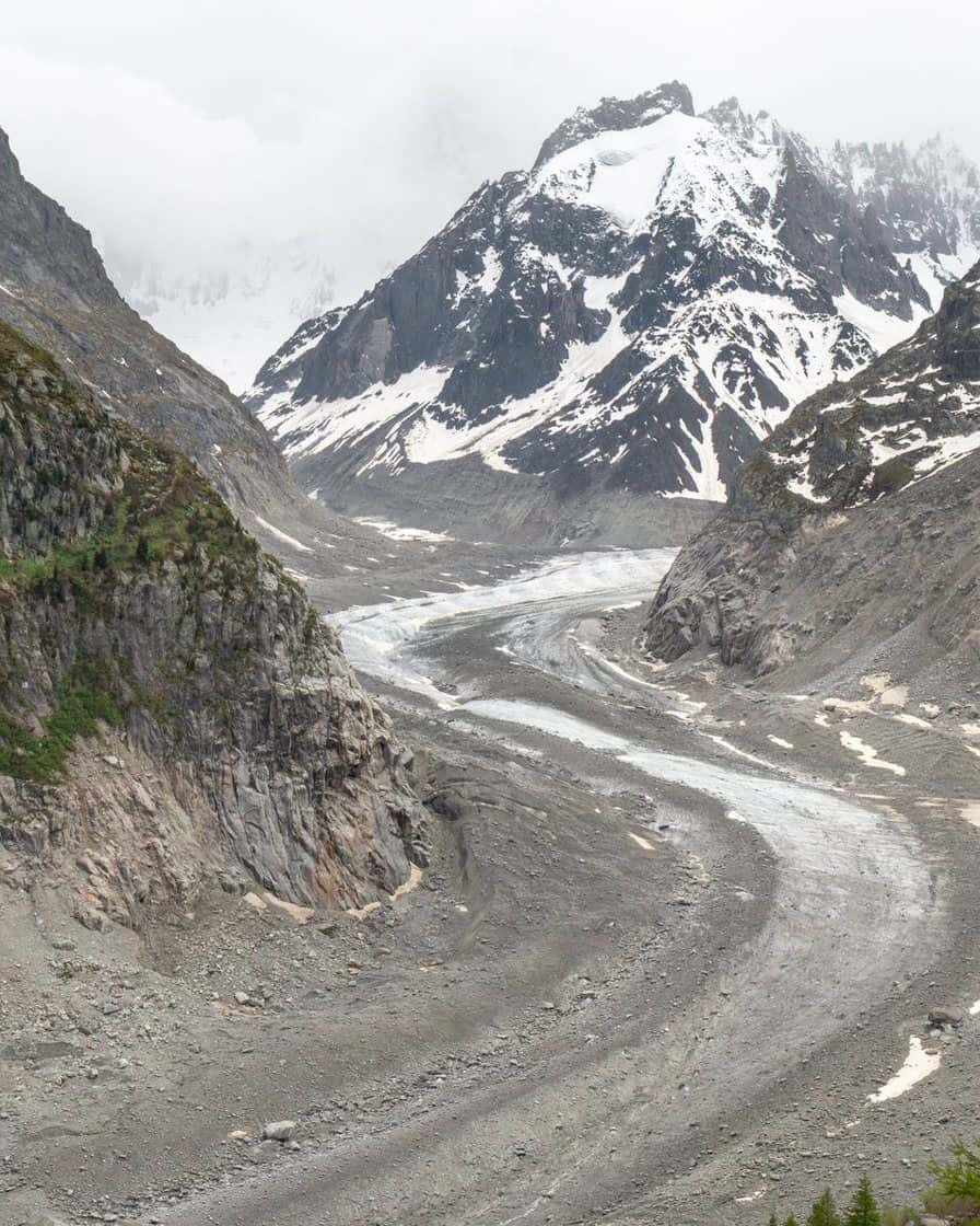 Glacier qui descend entre des versants rocheux, sommets enneigés au-dessus