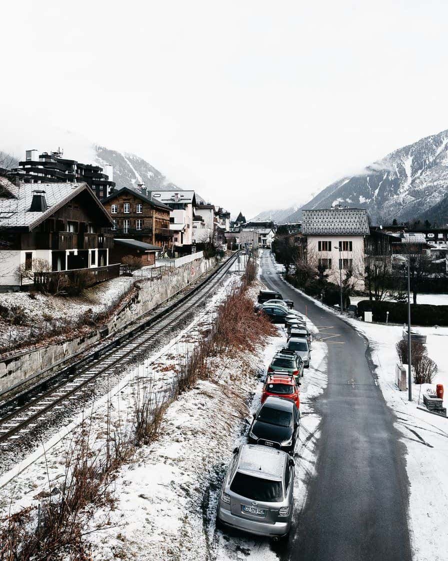 Village de la vallée de Chamonix sous la neige, voie ferrée et voitures garées le long de la route