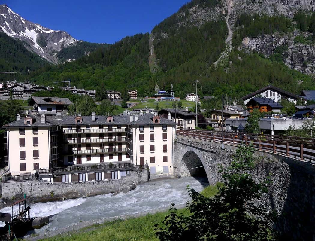 The hamlet of Dolonne in Courmayeur on the Dora Baltea, a hotel and stone houses below the wooded slopes on the Italian side