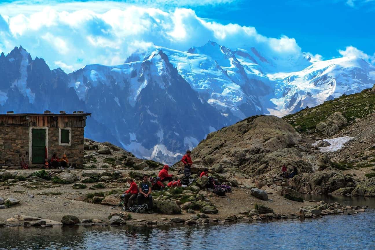 Hikers resting by the refuge at Lac Blanc above Chamonix, facing the Aiguille du Midi and the Mont Blanc massif under summer clouds