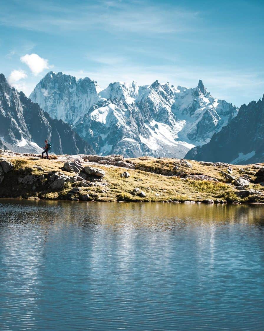 A hiker on the shore of a high-altitude lake facing the snowy needles of the massif